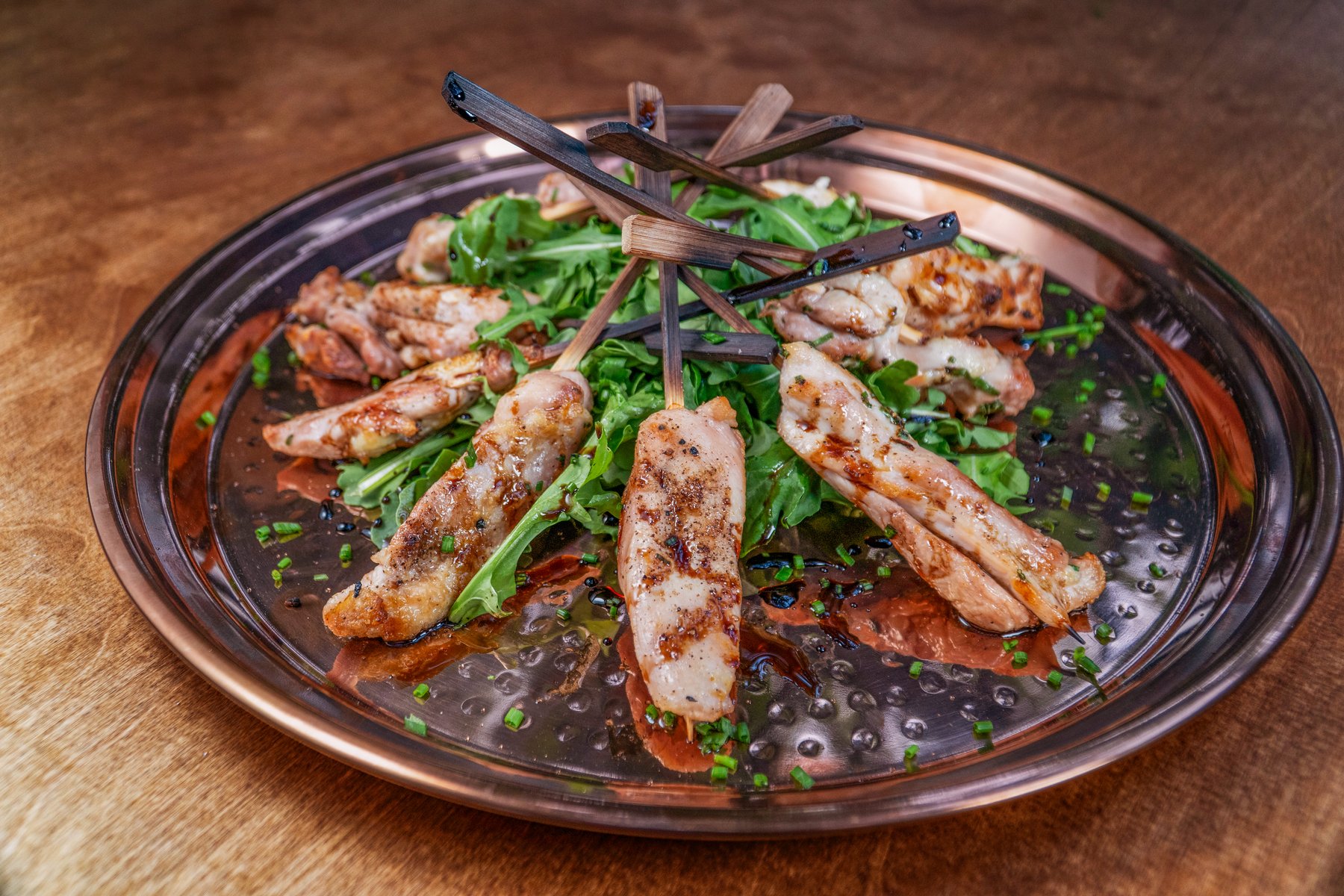 Grilled skewers on a copper platter with fresh arugula